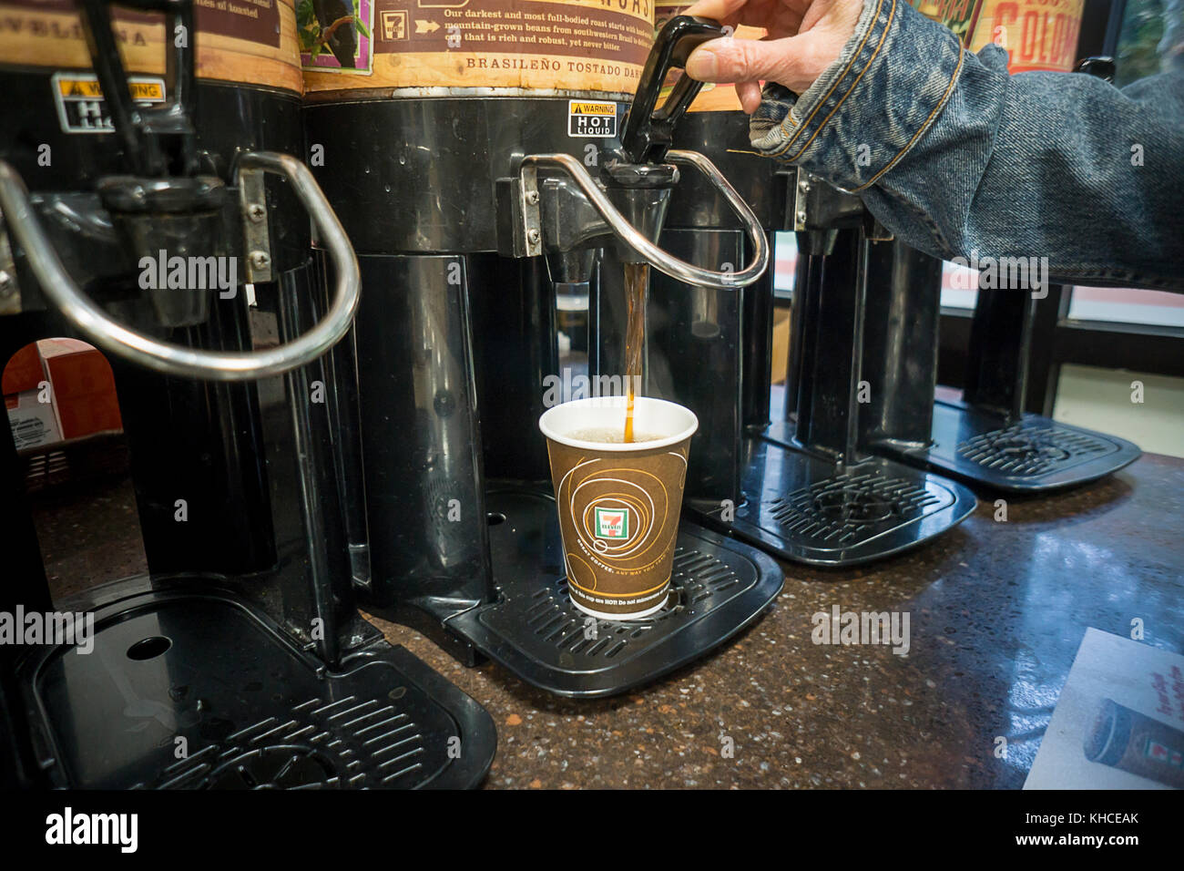 A coffee drinker fills up her cup with Brazilian Roast coffee in a 7-Eleven store in New York on Tuesday, November 8, 2017. Small coffee shops and cafes, which procreated in the last few years due to the popularity of specialty coffee, are suffering as larger chains such as 7-Eleven, Dunkin' Donuts and even McDonald's get into the business of selling specialty coffees at prices lower than local shops. The ubiquity of the larger chains is also making it more convenient for consumers to get a decent coffee fix. (© Richard B. Levine) Stock Photo
