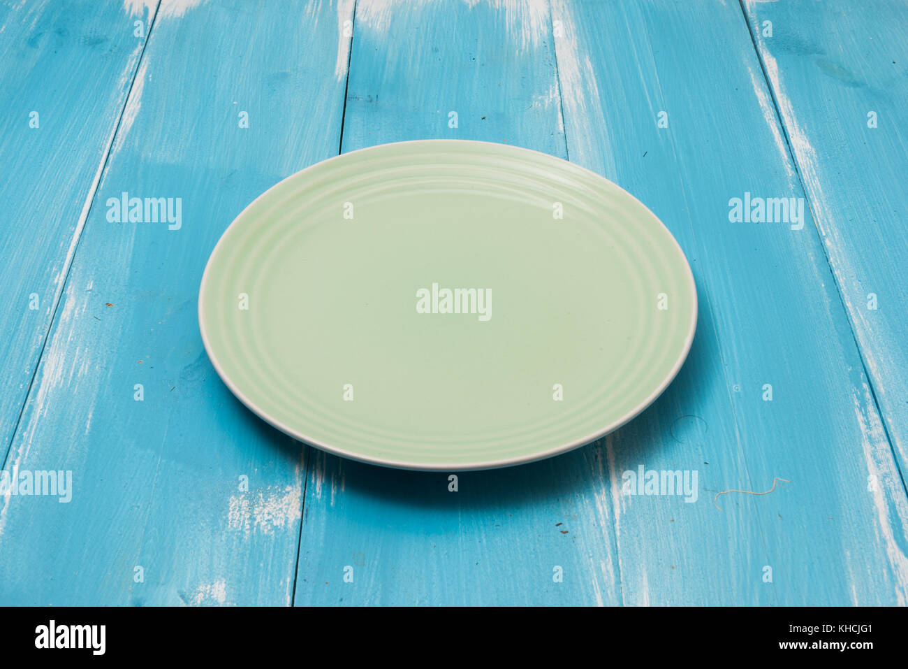 Green Round plate on blue wooden table with perspective side view Stock Photo