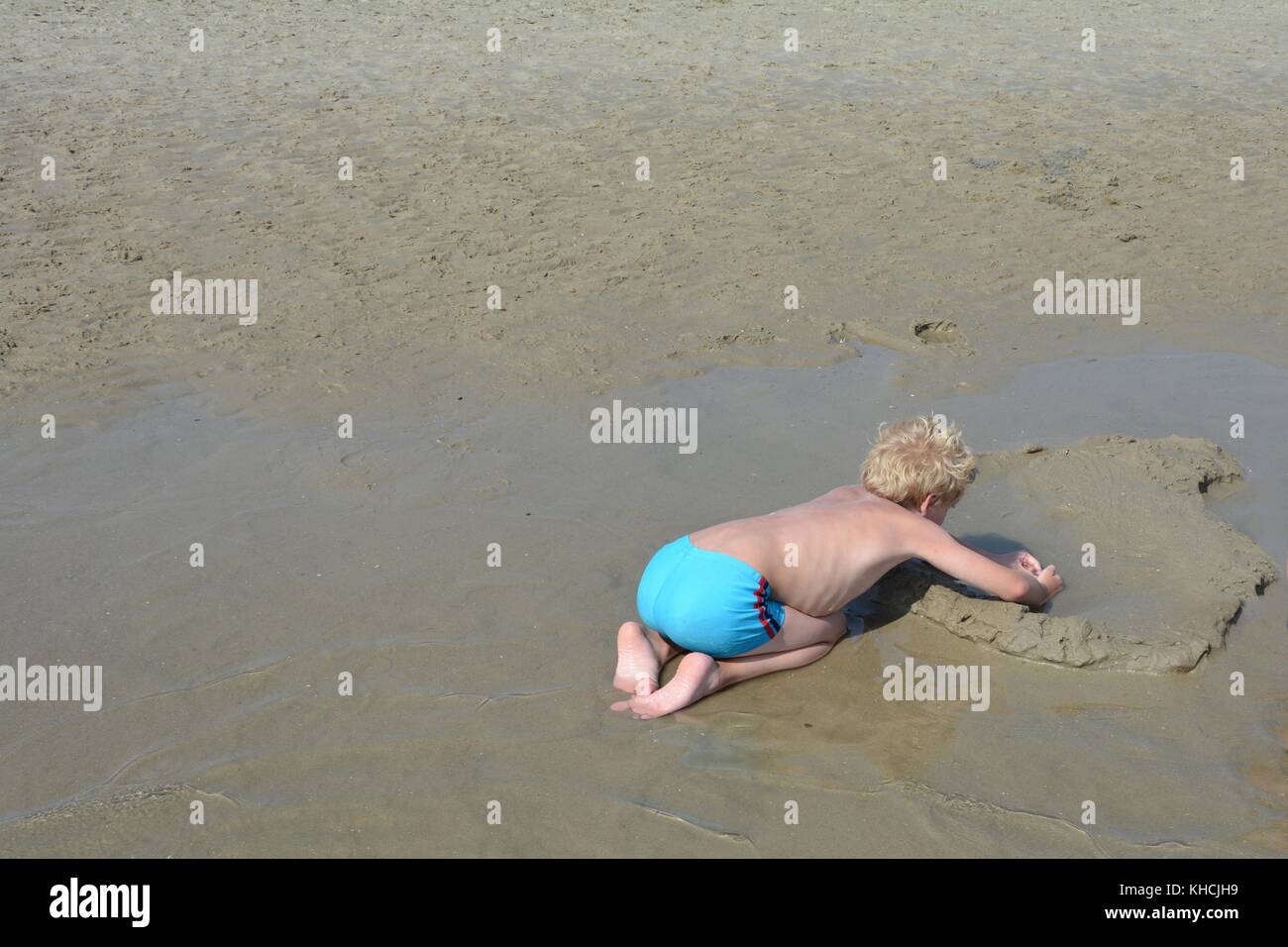 Small blond boy with swimming trunks plays in the sand on the beach Stock Photo