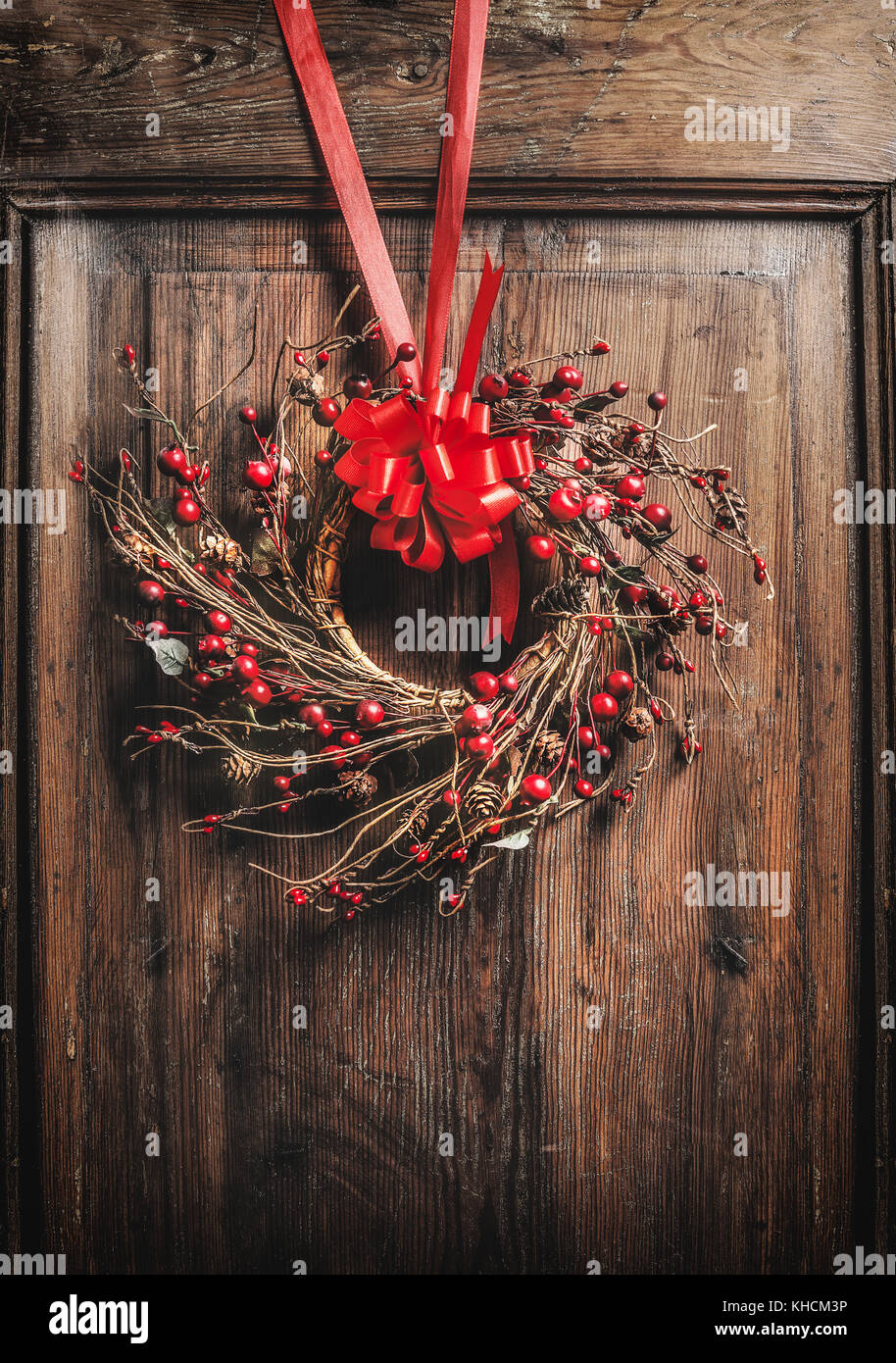 Handmade Christmas wreath hanging on wooden door with red ribbon and berries , front view Stock Photo