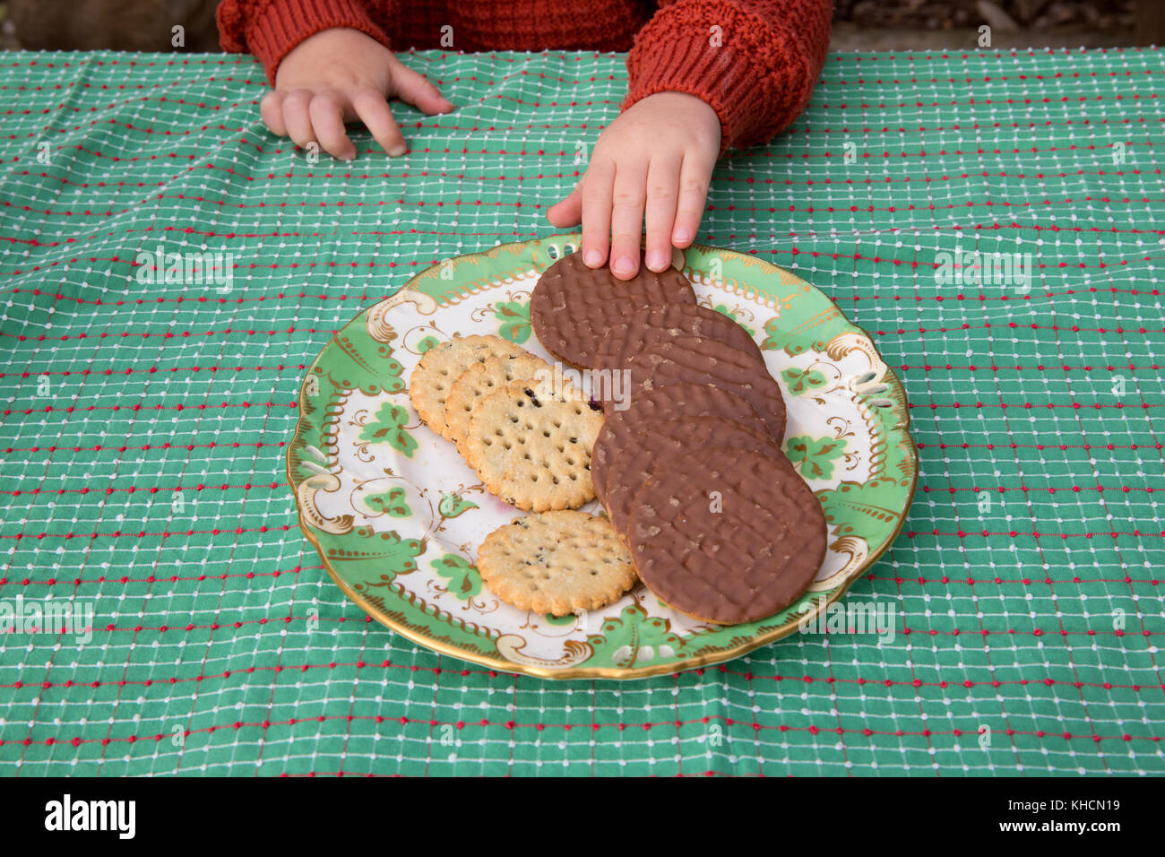 Boy at table choosing chocolate biscuit from plate, cropped detail Stock Photo