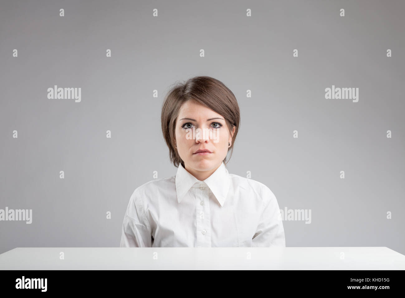 serious inexpressive woman portrait in front of an work table on a gray background with lots of copyspace Stock Photo