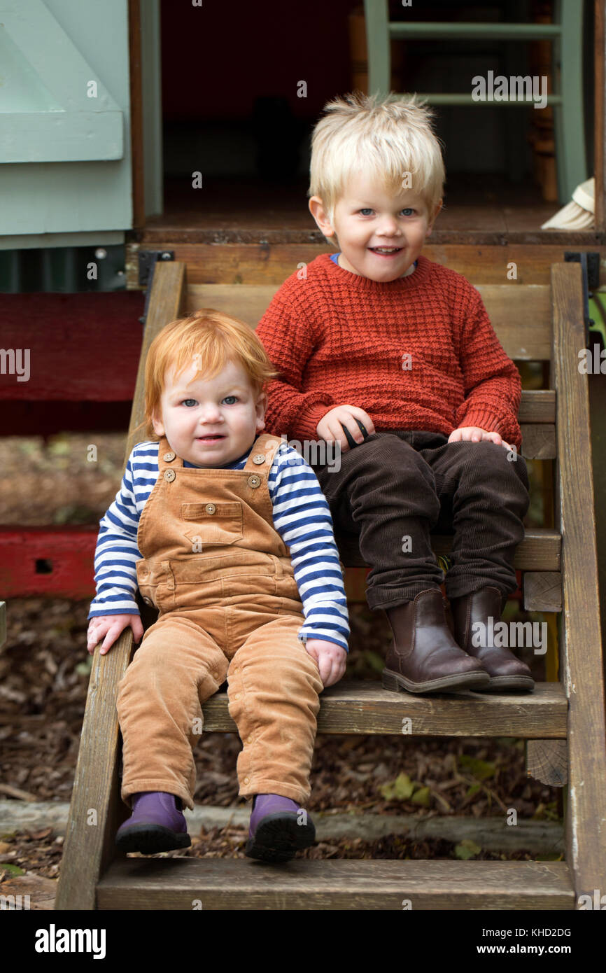 Male toddler and brother sitting on steps of traditional gypsy caravan, portrait Stock Photo