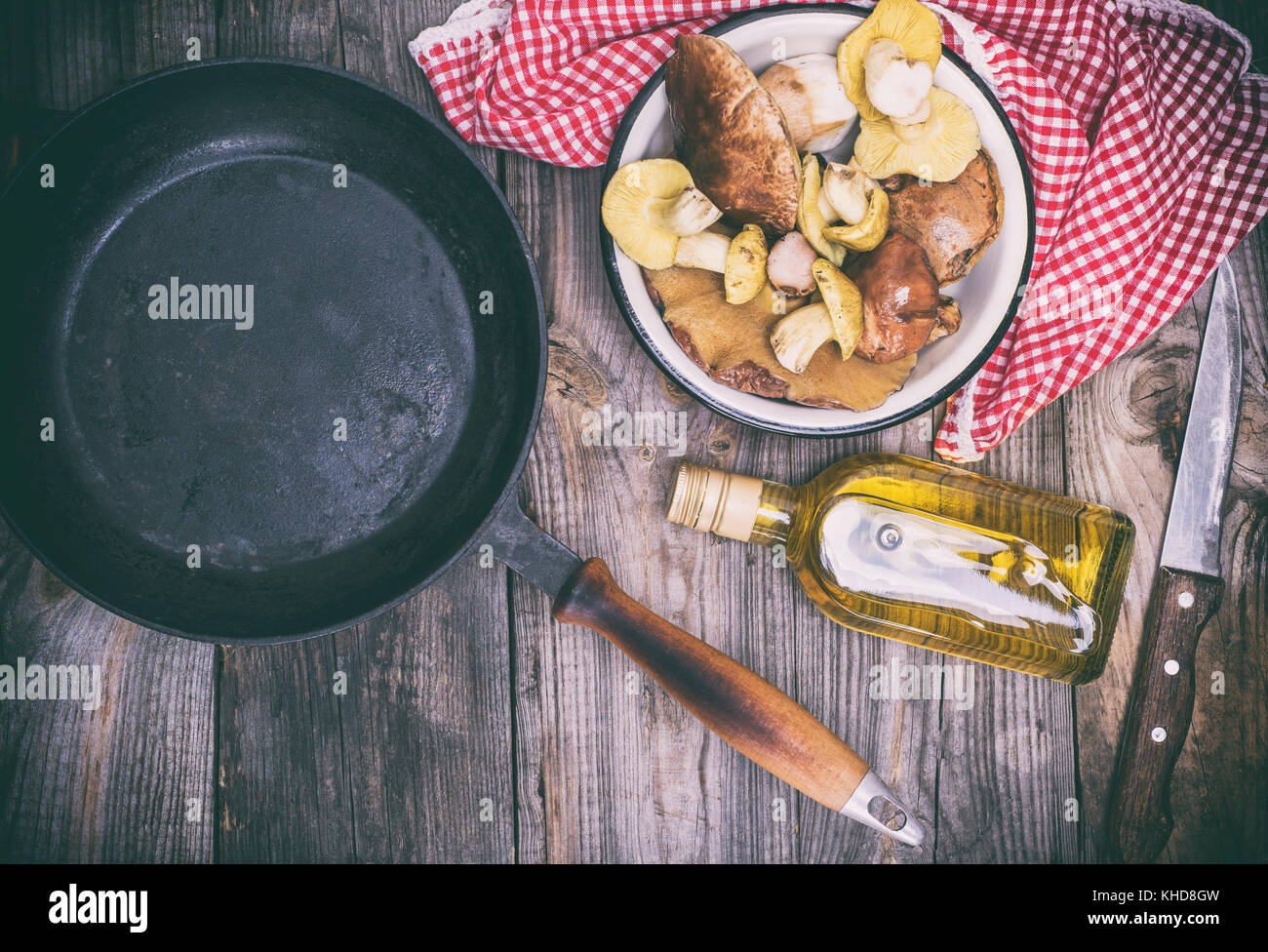 fresh edible wild mushrooms, olive oil and black round cast-iron frying pan on a gray wooden background, top view Stock Photo