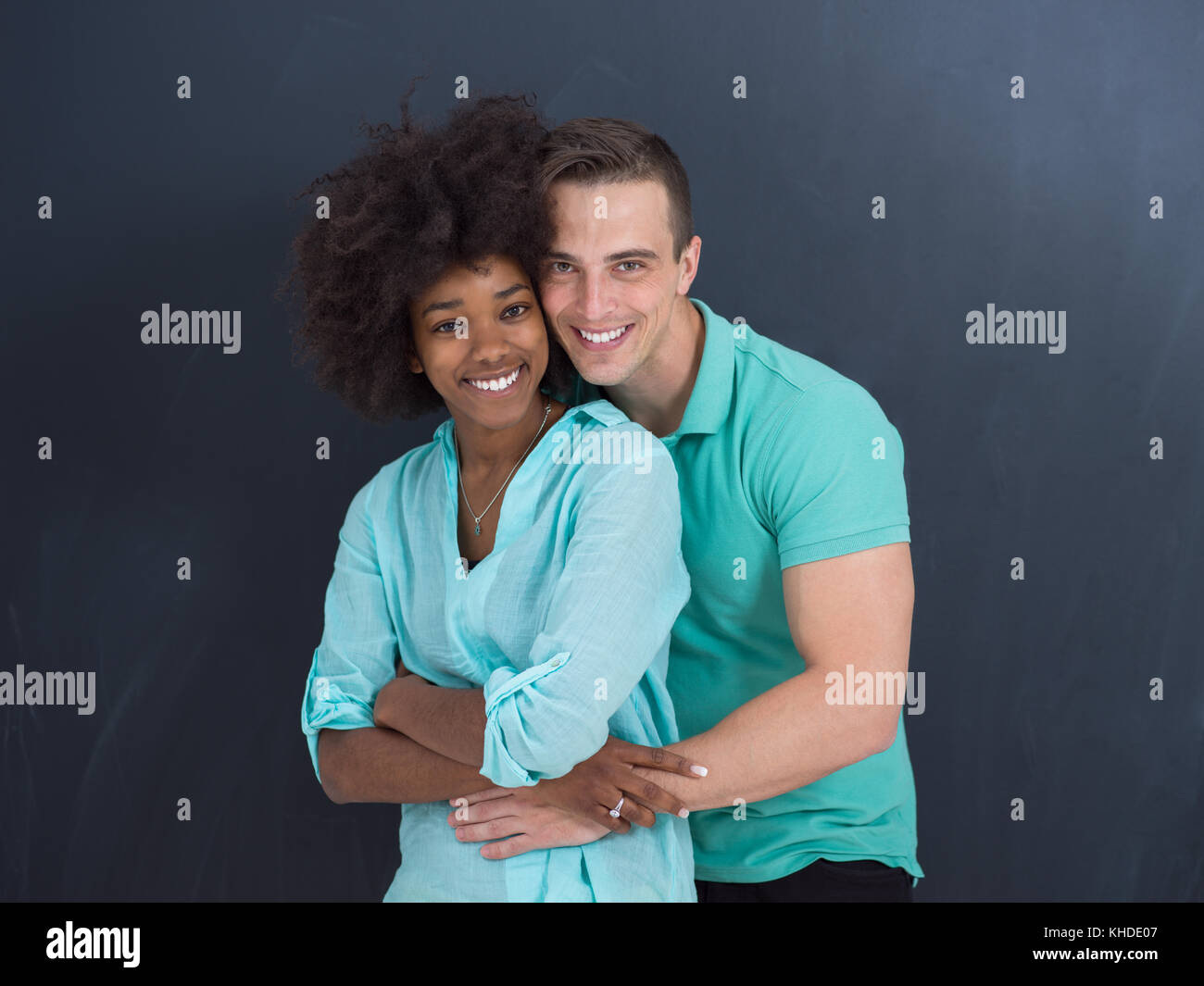 Young happy multiethnic couple laughing and hugging in front of gray ...