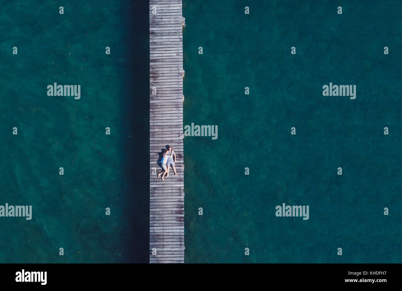 travel background with copy space, drone aerial view of honeymoon romantic couple lying down on wooden pier, beach holidays Stock Photo