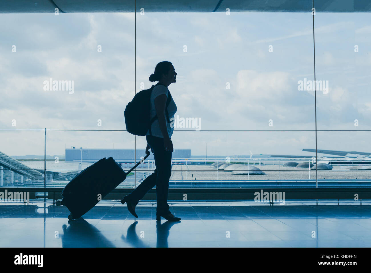 departures in airport, silhouette of woman walking with suitcase, travel background with copy space Stock Photo