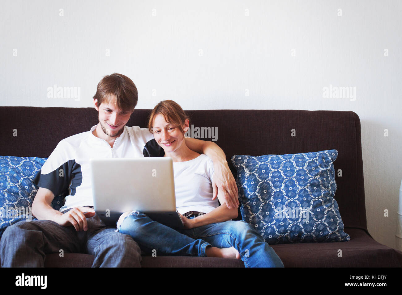 young couple looking at computer and smiling, family sitting on the couch at home Stock Photo