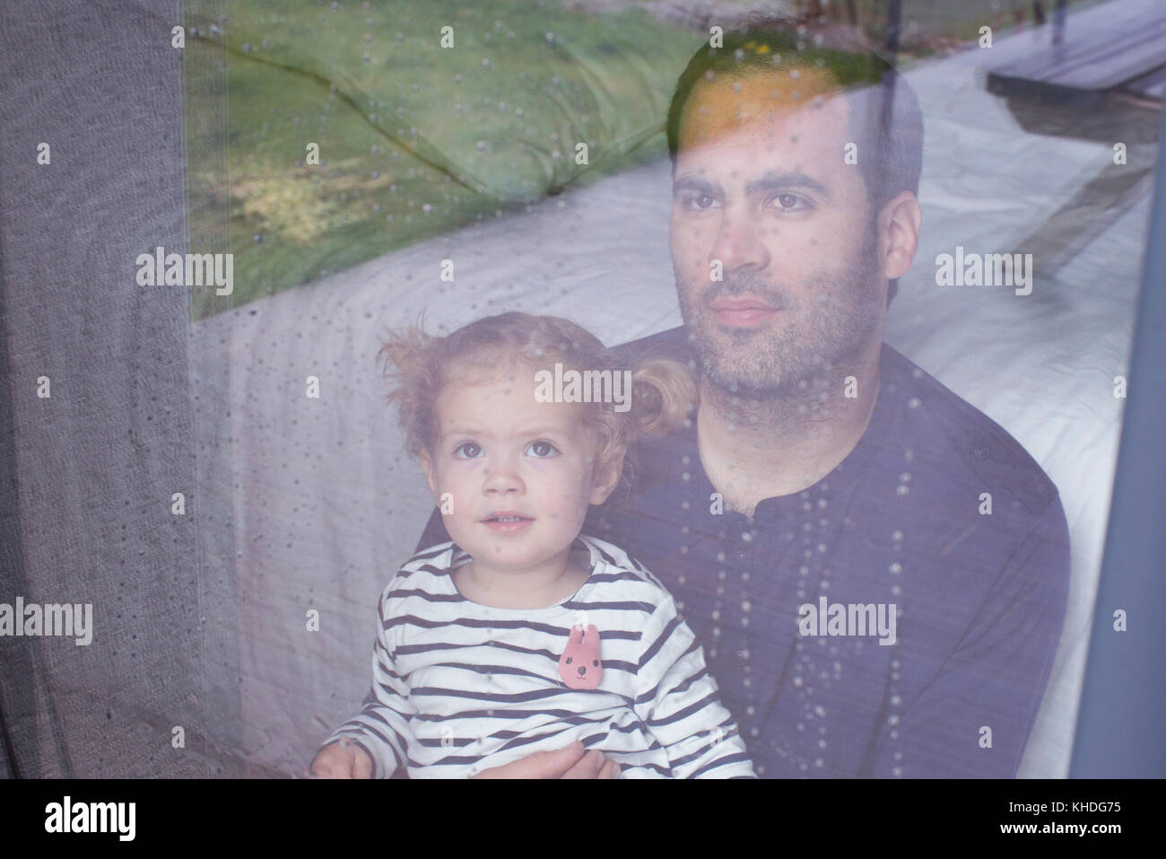 Man with young child looking through window watching rain fall Stock Photo