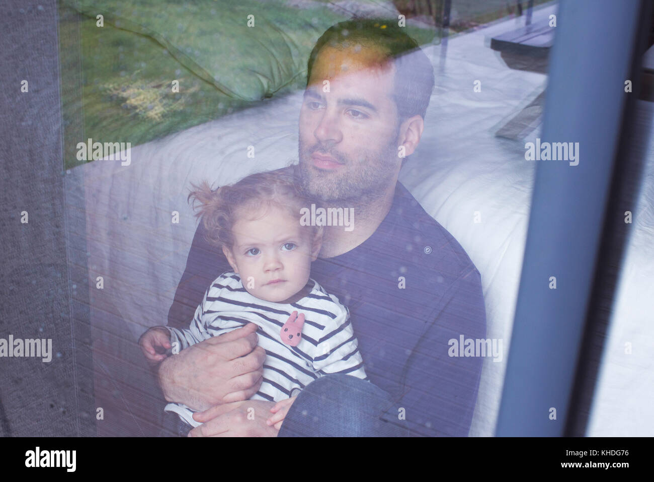 Man with young child looking through window watching rain fall Stock Photo