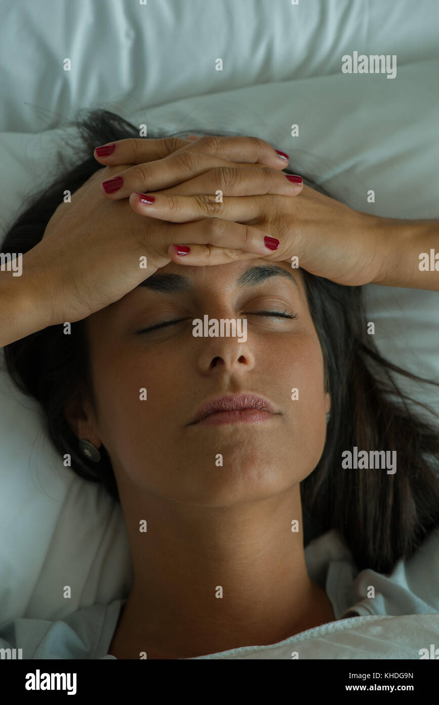 Woman lying in bed with hands on forehead Stock Photo