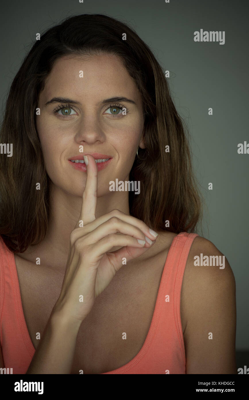 Young woman smiling with finger held to lips Stock Photo