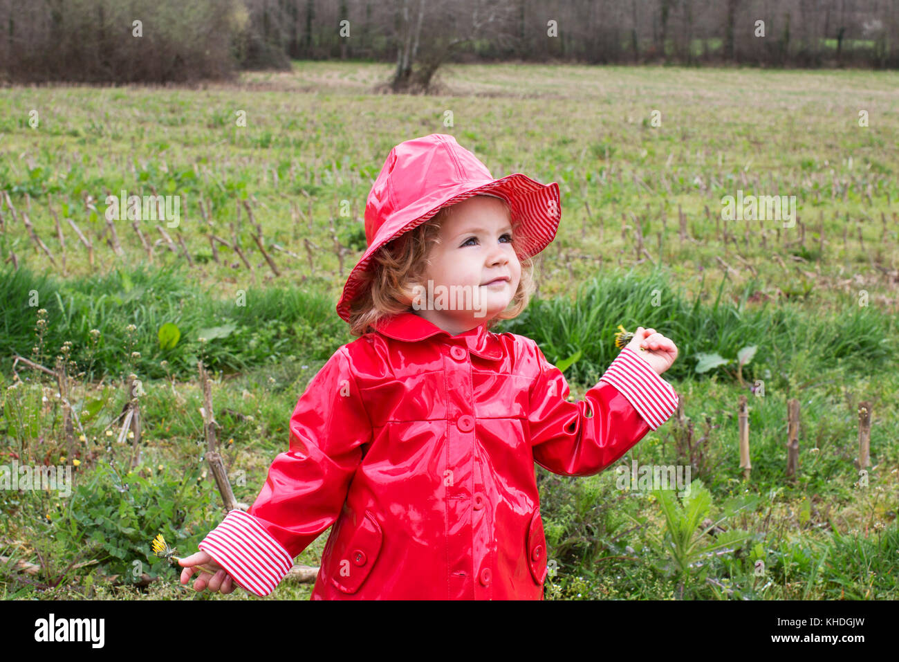 Little girl wearing rain gear playing in field Stock Photo