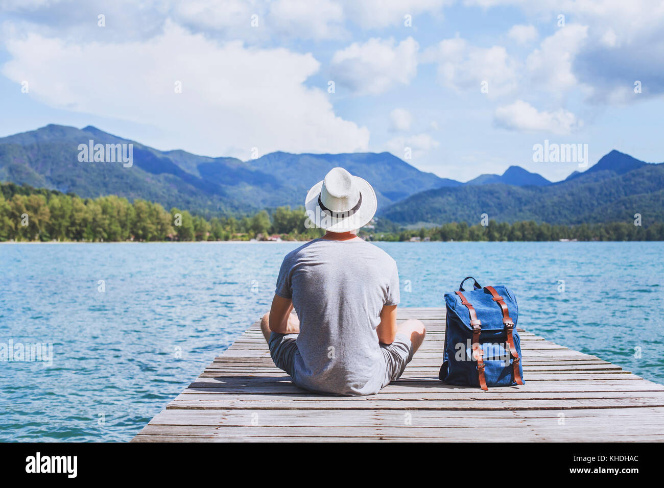 summer travel, young romantic man tourist wanderlust sitting on wooden pier Stock Photo
