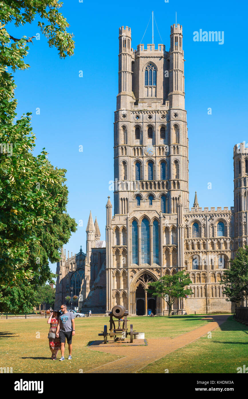 Ely Cathedral tower, on a summer afternoon a young couple walk through Palace Green on the west side of Ely Cathedral, Cambridgeshire, England, UK. Stock Photo