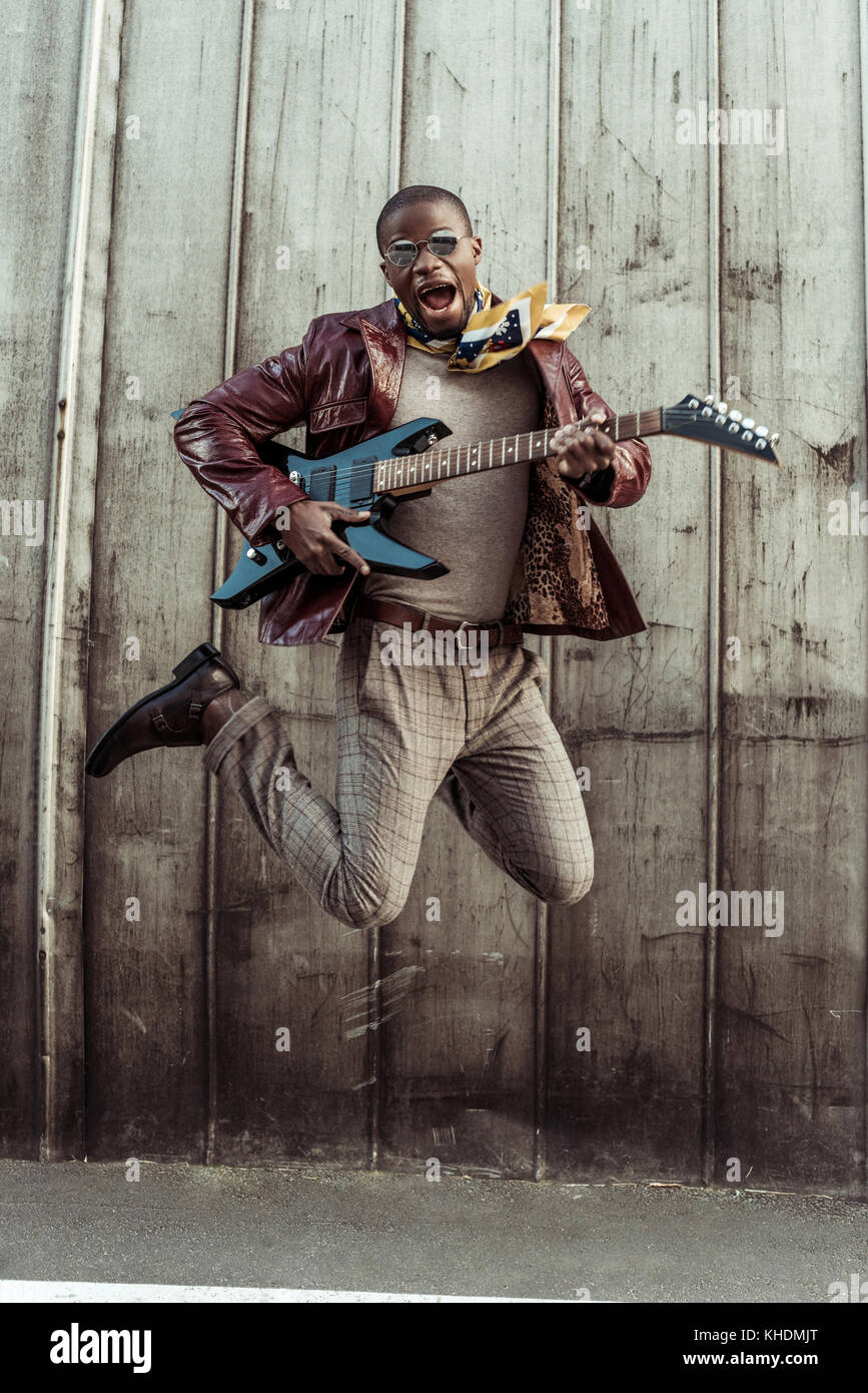 Stylish man jumping with guitar Stock Photo