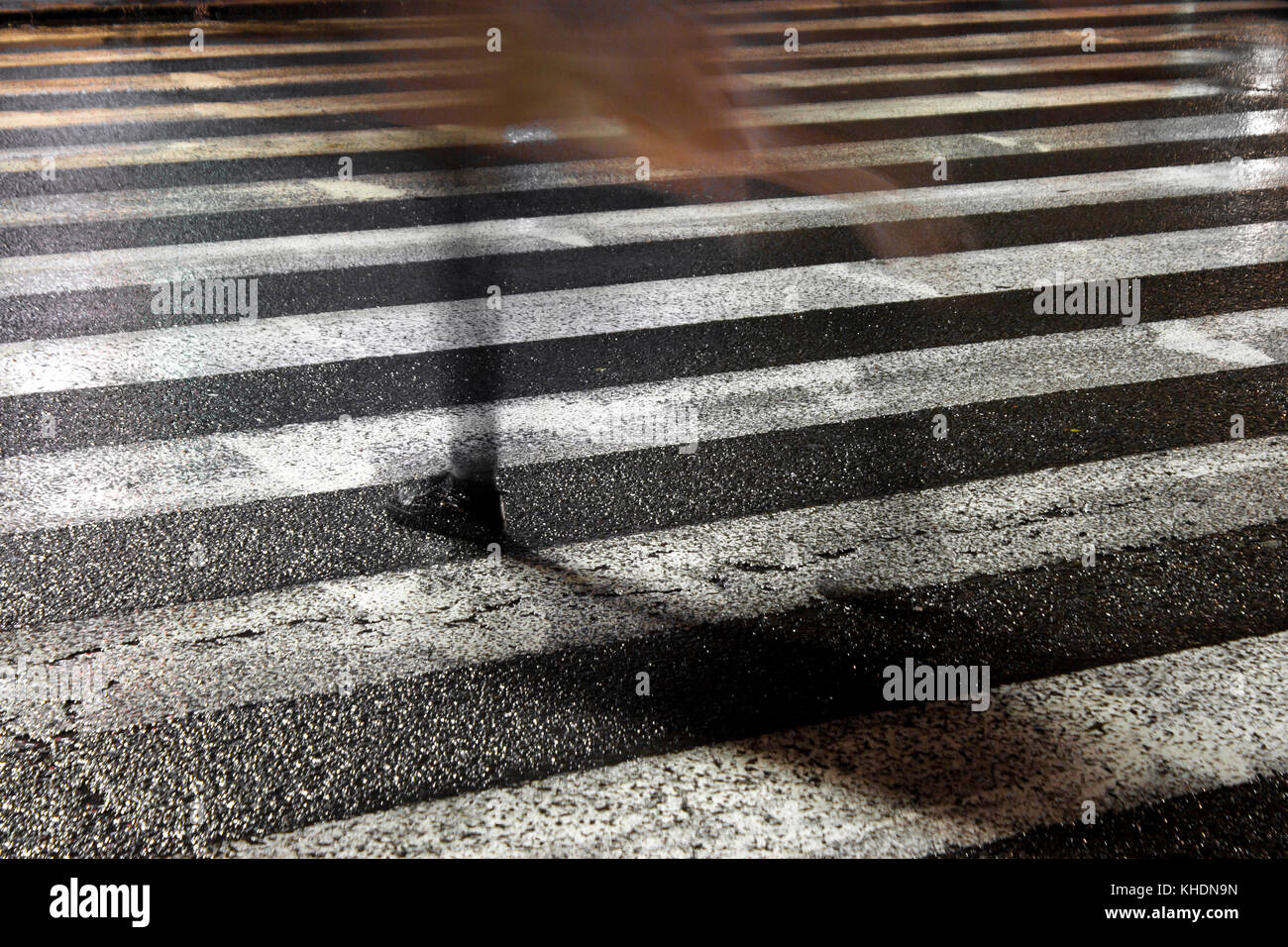 Rainy city street reflections: One young fragile female disappearing while crossing the wet street in the sparkling night Stock Photo
