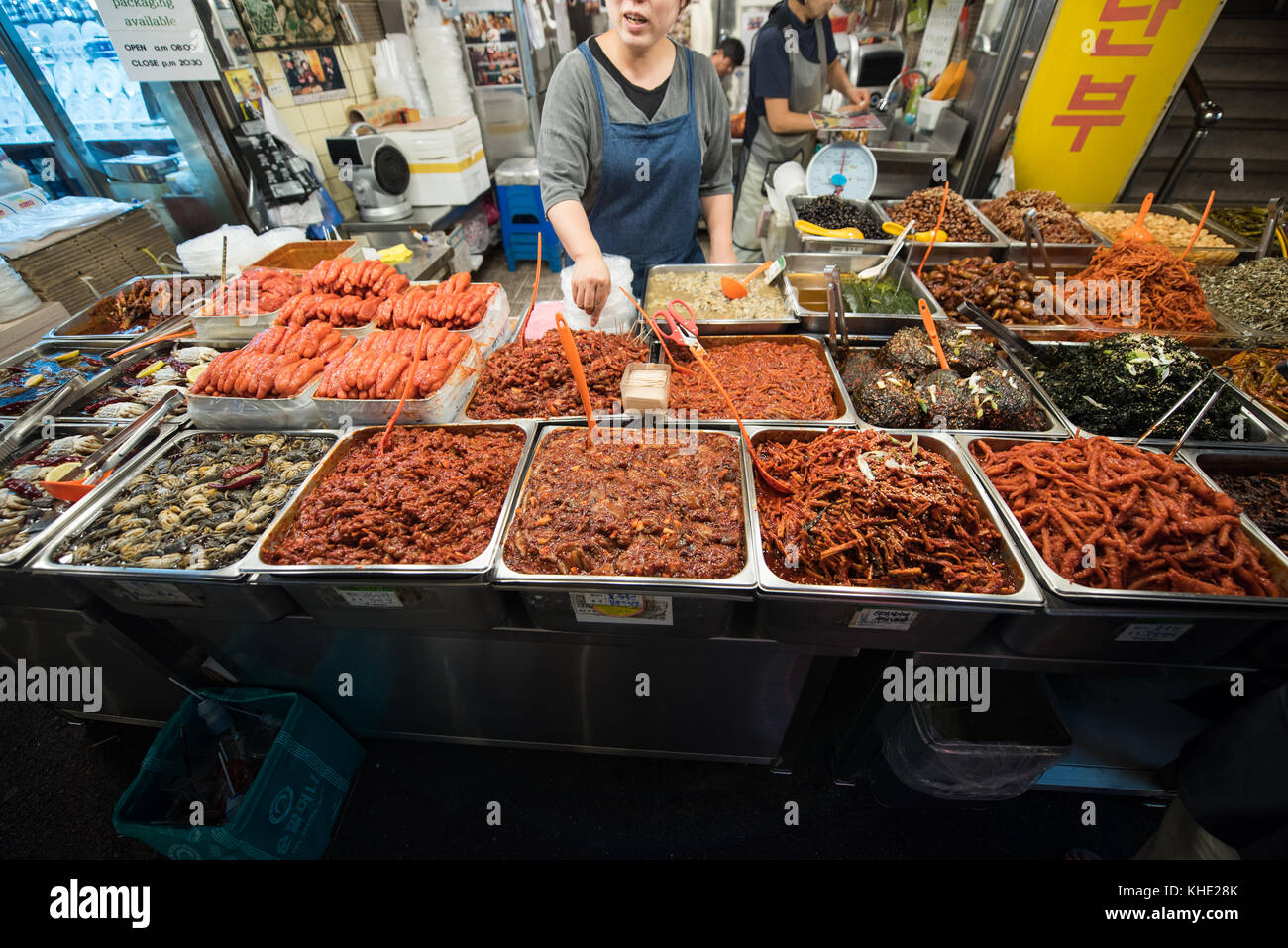 A Korean woman running a store selling korean side dishes, pointing at a specific food in Kwangjang Market, Seoul. Stock Photo