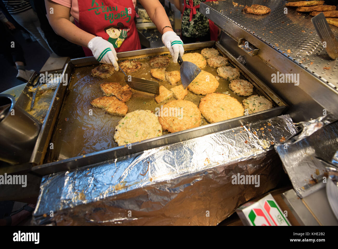 A Korean lady prepares a korean street food called 'Bindaeduk' by frying ground up Mung bean batter in a shallow hot oil. Kwangjang Market, Seoul 2017. Stock Photo