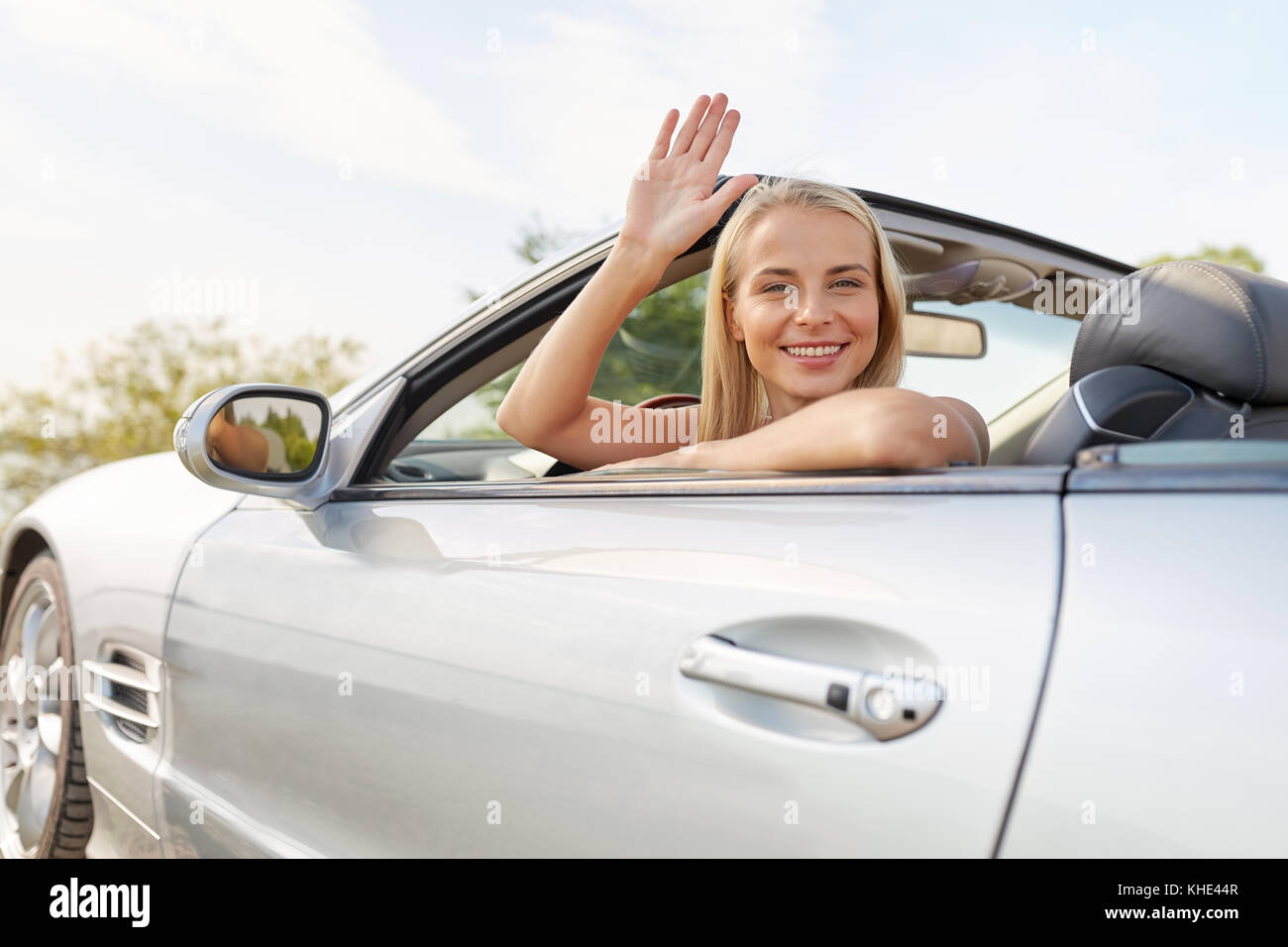 Happy blonde woman with flowing hair waving in a convertible - wide 4