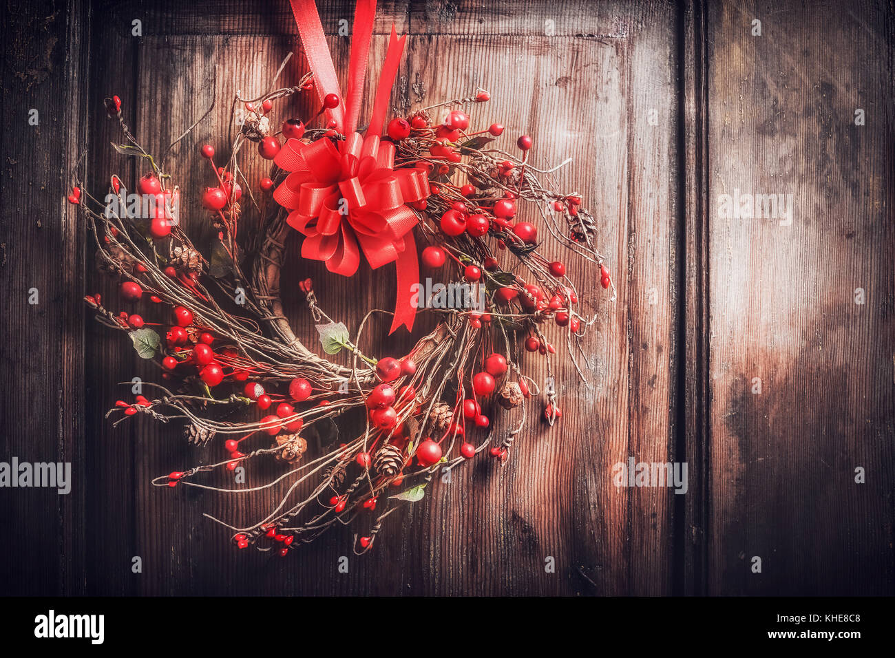 Handmade Christmas wreath hanging on dark wooden door with red ribbon ...