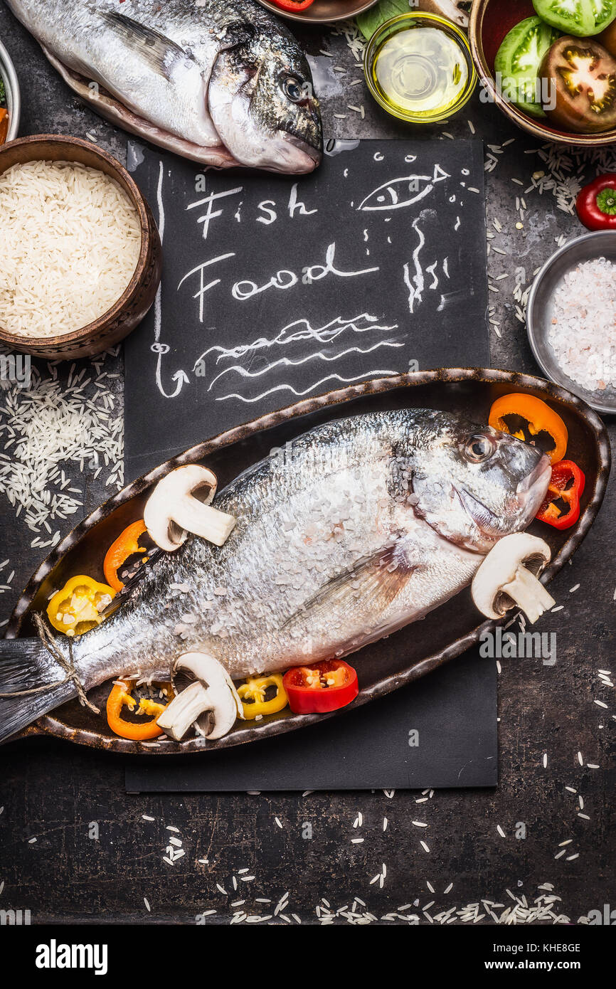 Fish food text with raw dorado, rice and vegetables cooking ingredients on dark rustic background, top view. Healthy food or diet food concept. Stock Photo