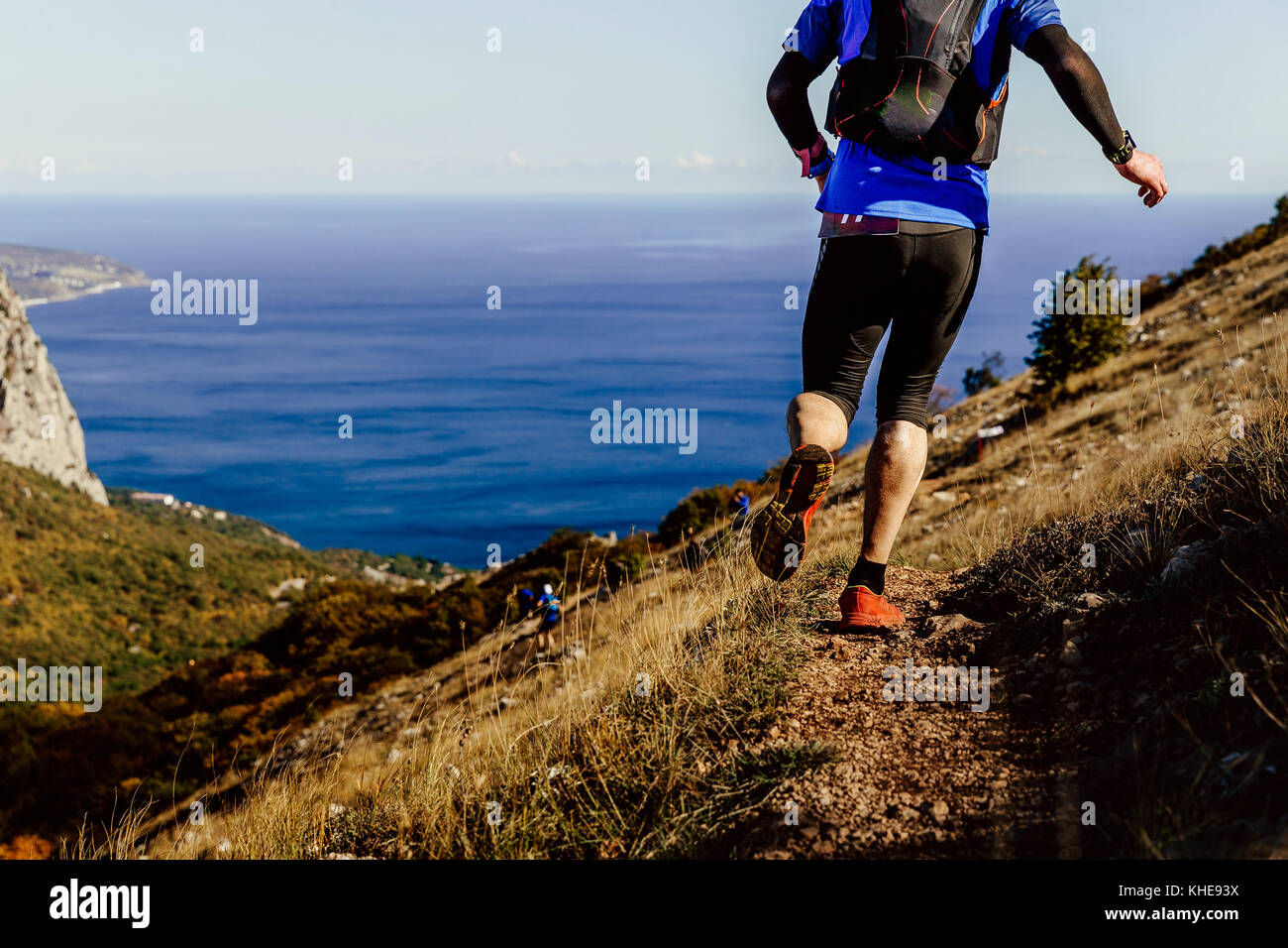 back legs of male athlete running mountain trail in background sea Stock Photo