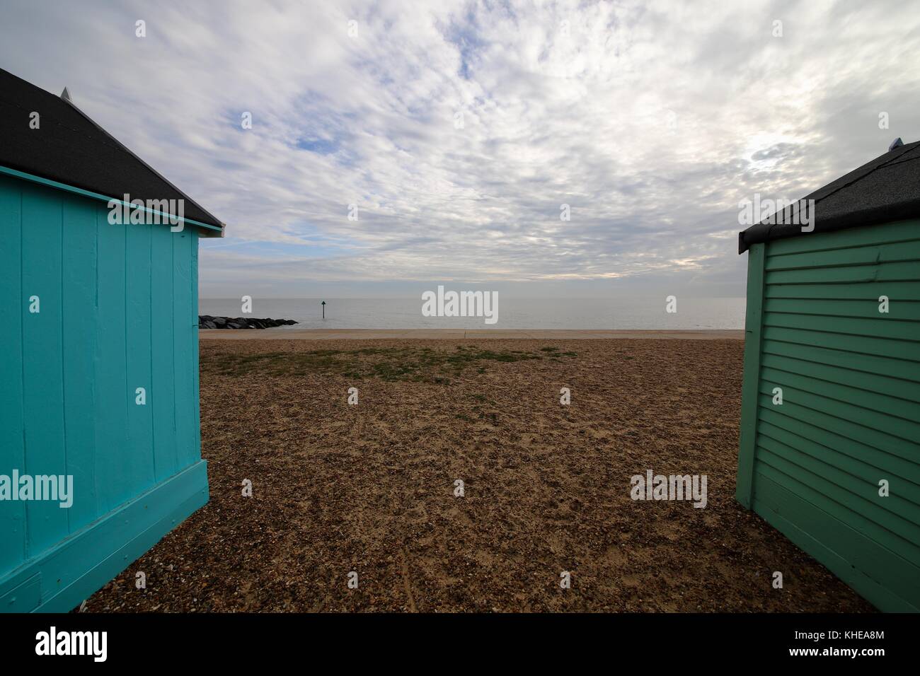 The view onto the shingle beach and the North Sea from between two beach huts. One hut has vertical boards the other has horizontal. Felixstowe, UK. Stock Photo