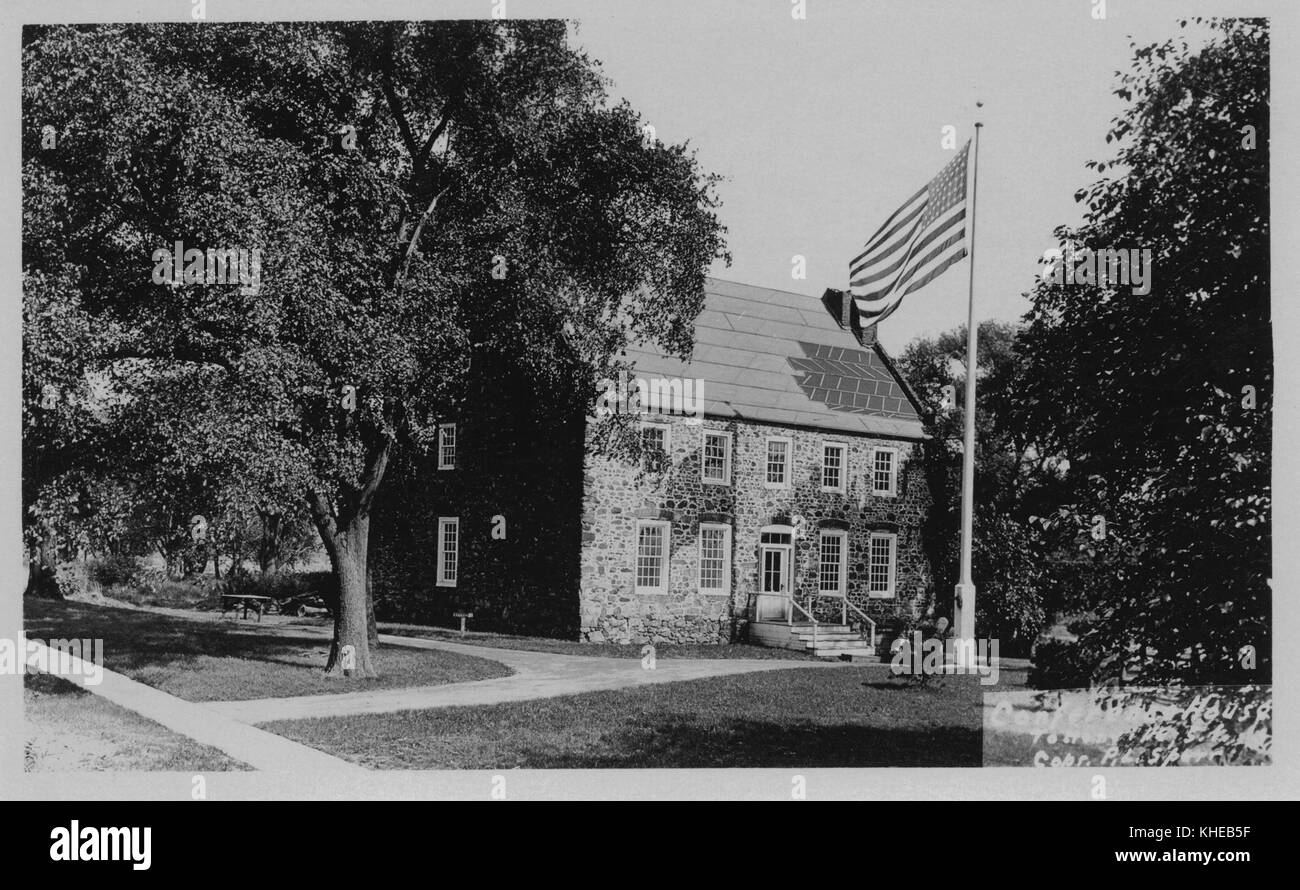 An old postcard picture of The Conference House, corner view of the stone house showing the front and right side, flag pole with raised flag in the front yard, a full grown tree with lots of foliage on the building's right side lawn, Richmond, Staten Island, New York, 1900. From the New York Public Library. Stock Photo