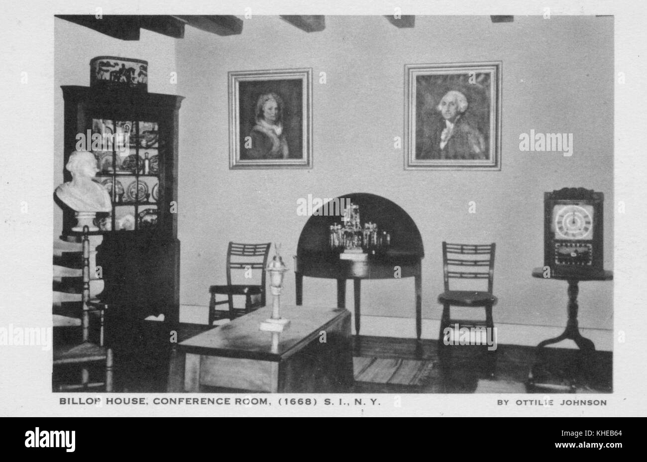 An old postcard picture of the Conference Room in Billop House, showing a wall hanged with two framed portraits of a man, two chairs set by the wall one right below each portrait, a half-moon side table set between the chairs, a man's bust mounted on the left side of the room, a wooden cabinet full of china standing on the left wall, and a rectangular low table set on the center of the room, Staten Island, New York, 1900. From the New York Public Library. Stock Photo