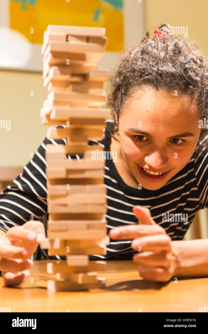 Young woman plays Jenga, stacking a tower with wooden blocks, concentrated Stock Photo