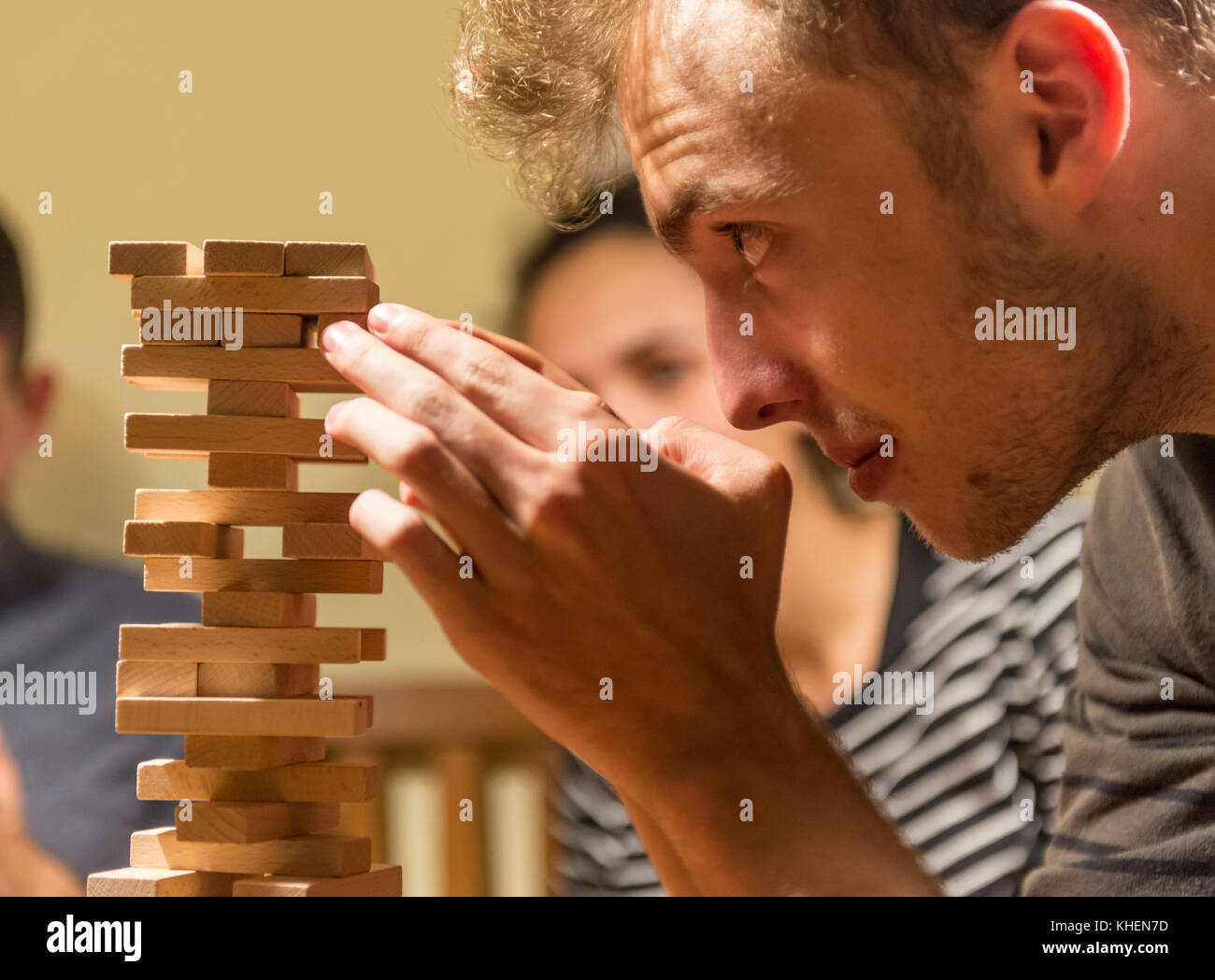 Young man plays Jenga, stacking a tower with wooden blocks, concentrated Stock Photo