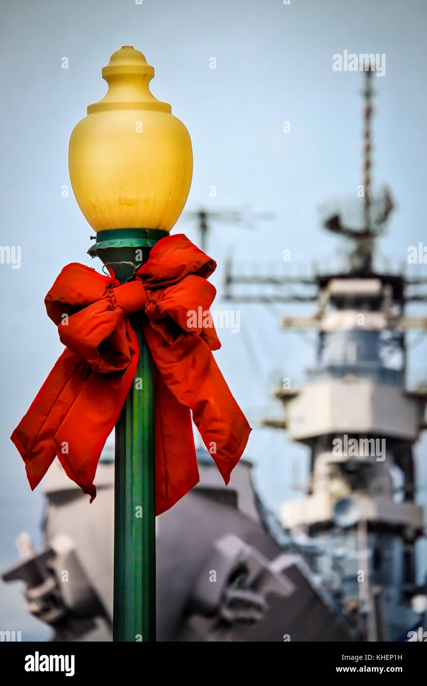 A street lamp decorated for Christmas with a US Navy warship in the background. Stock Photo
