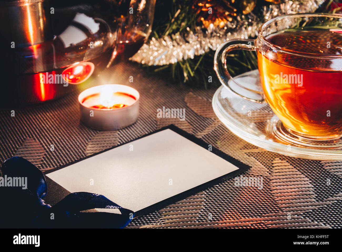 Invitation card to the party with empty space on the table near christmas tree, candle and cup of hot tea. Cosy evening Stock Photo