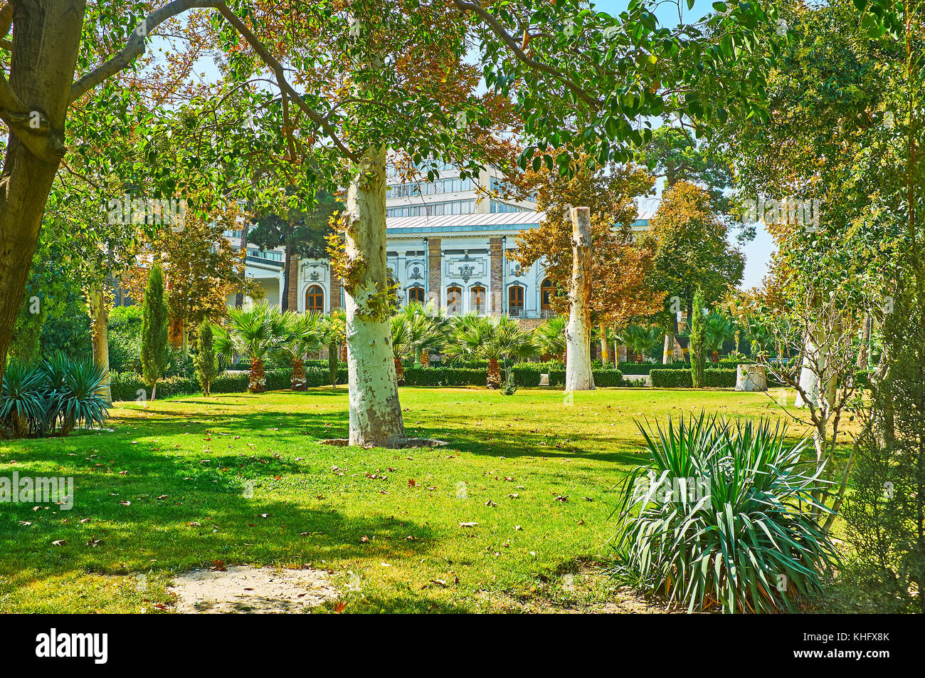 The walk among the palms and sycamore trees of Golestan garden with a view on white wall of Abyaz palace through the branches, Tehran, Iran. Stock Photo
