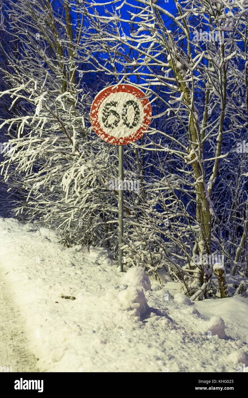 Early winter evening with snow, 60 km/t road sign covered in snow Stock Photo