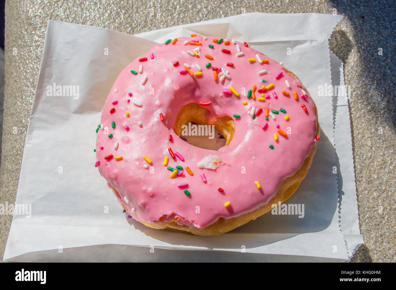 large pink iced donut on a paper bag Stock Photo