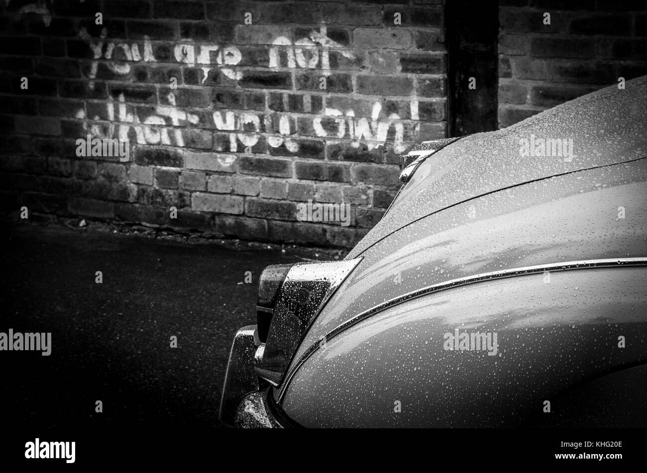 Jaguar Mk2 parked in a industrial scene with graffiti written on the wal quoting 'YOU ARE NOT WHAT YOU OWN' The picture is in back on white like Morse Stock Photo