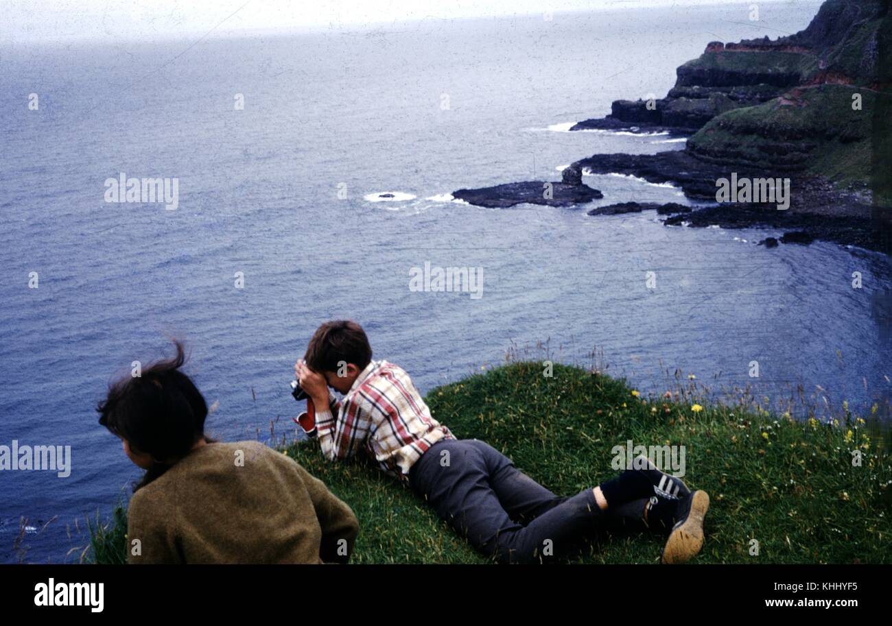 Brother and sister leaning over a sea cliff and taking photos on the North Ireland coast, near the Devil's Causeway, Ireland, 1961. Stock Photo