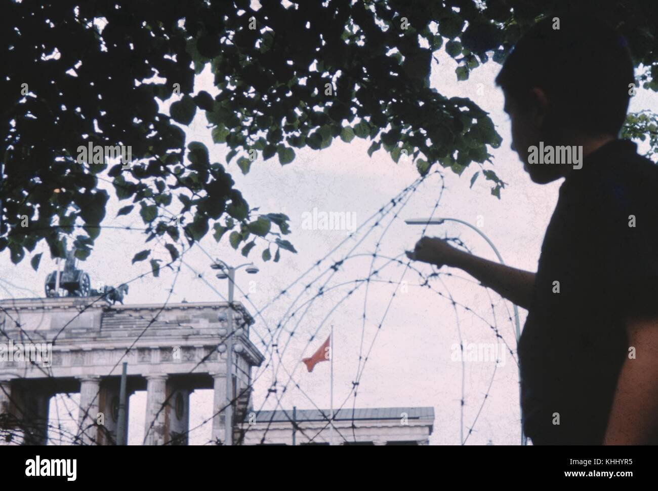 Child, seen in silhouette, reaching towards barbed wire marking the line between East Berlin and West Berlin, with buildings on the East Berlin side visible beyond the wire, Germany, 1961. Stock Photo
