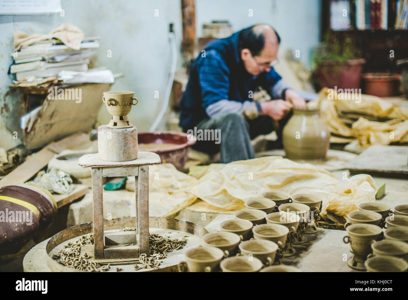 A Korean potter displays a freshly made cup while making another piece in the background in his pottery studio. Gyeongju, South Korea Stock Photo