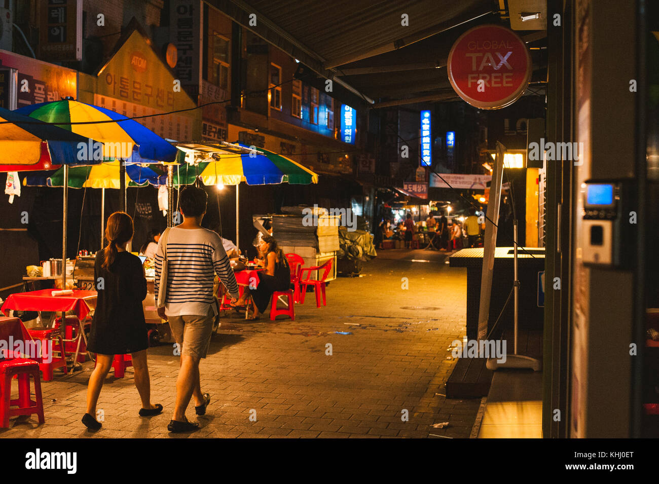 A shot of a couple walking past a street food stall at night in Namdaemun market, Seoul, South Korea Stock Photo
