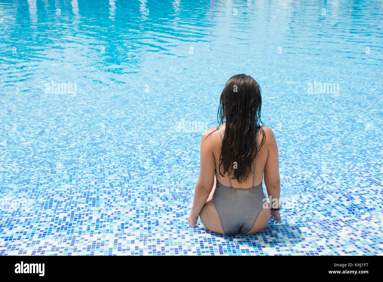 Rear view of a woman in bikini sat in the pool Stock Photo