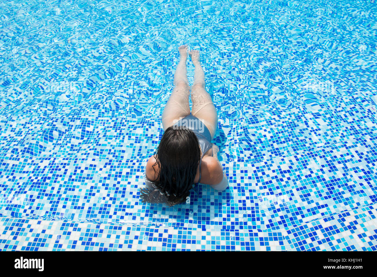 Rear view of a woman in bikini sat in the pool Stock Photo