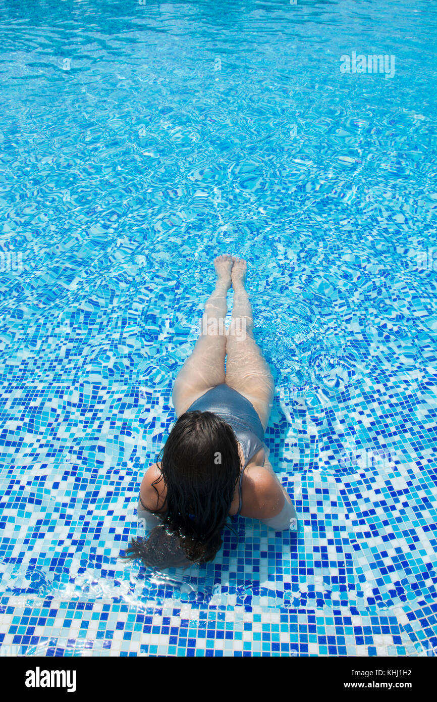 Rear view of a woman in bikini sat in the pool Stock Photo