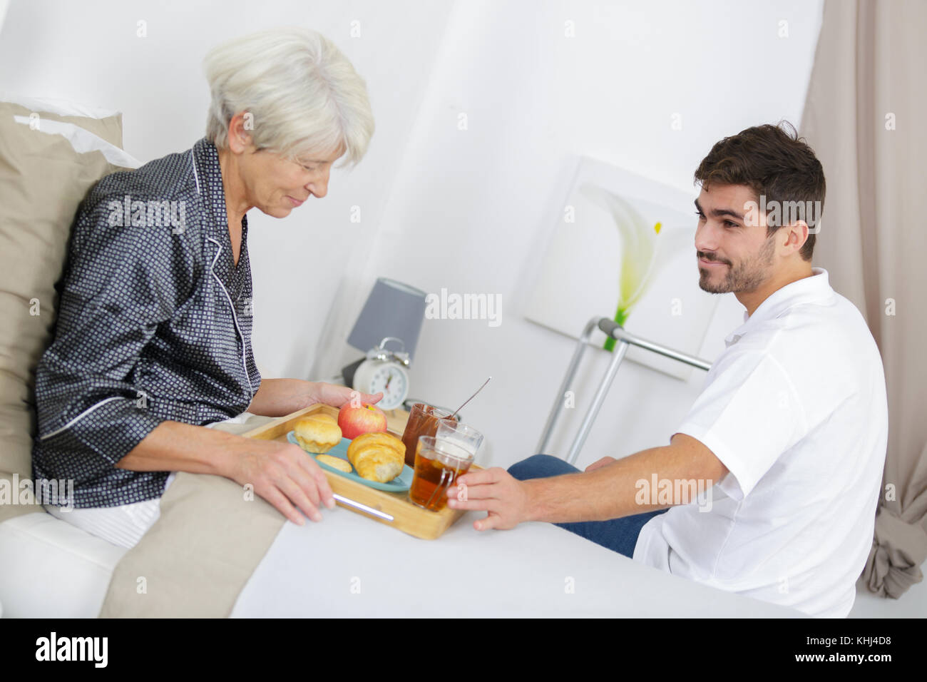 Young man serving breakfast in bed to elderly lady Stock Photo