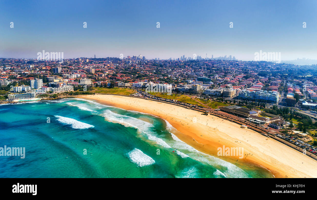 Wave breaks and surf on clear sand of famous Australian Sydney Bondi beach in aerial view with city CBD in background. Stock Photo