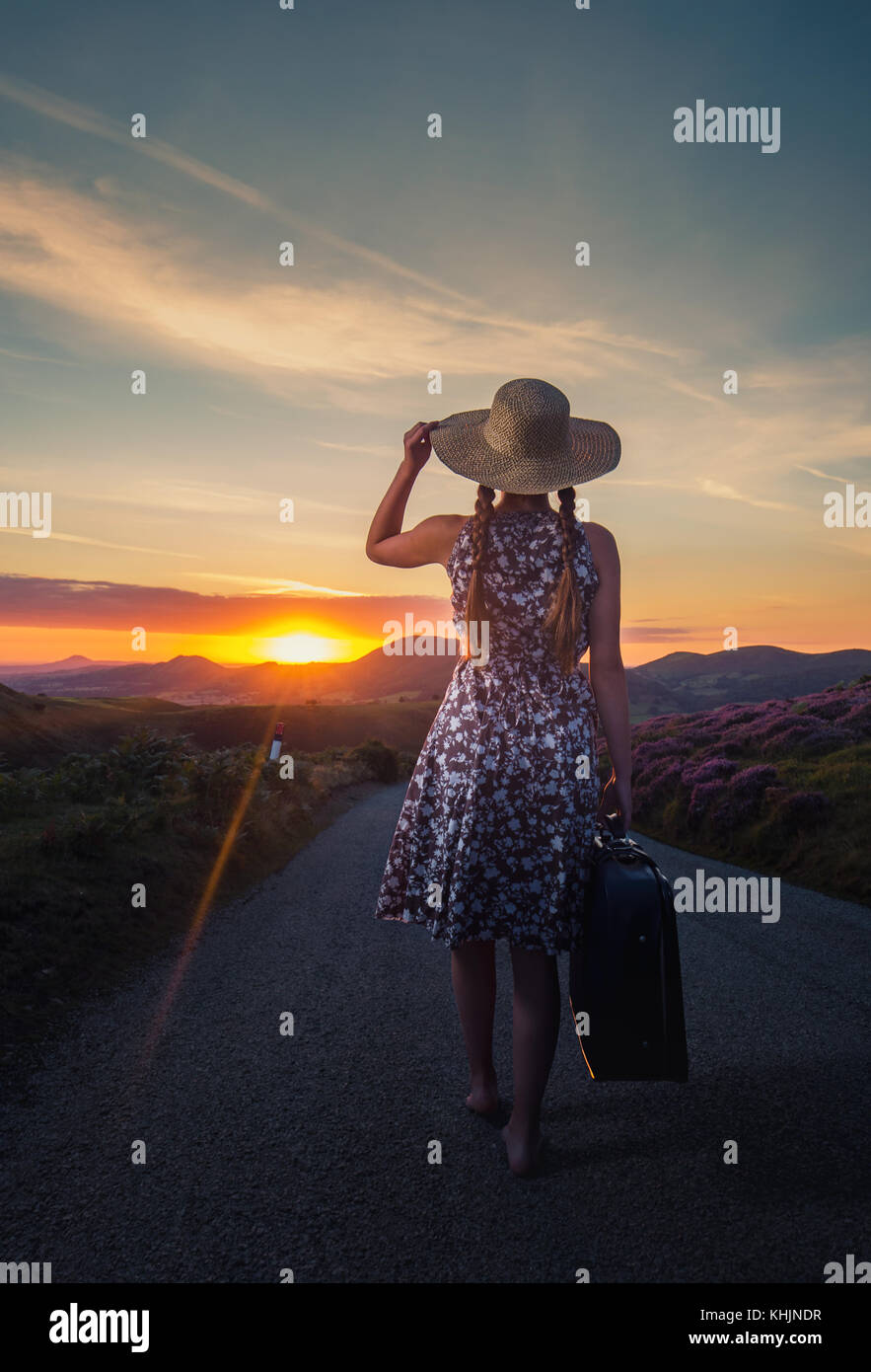 Girl with a Suitcase Looking at Beautiful Sunrise Walking on Asphalt Road in Mountains Stock Photo
