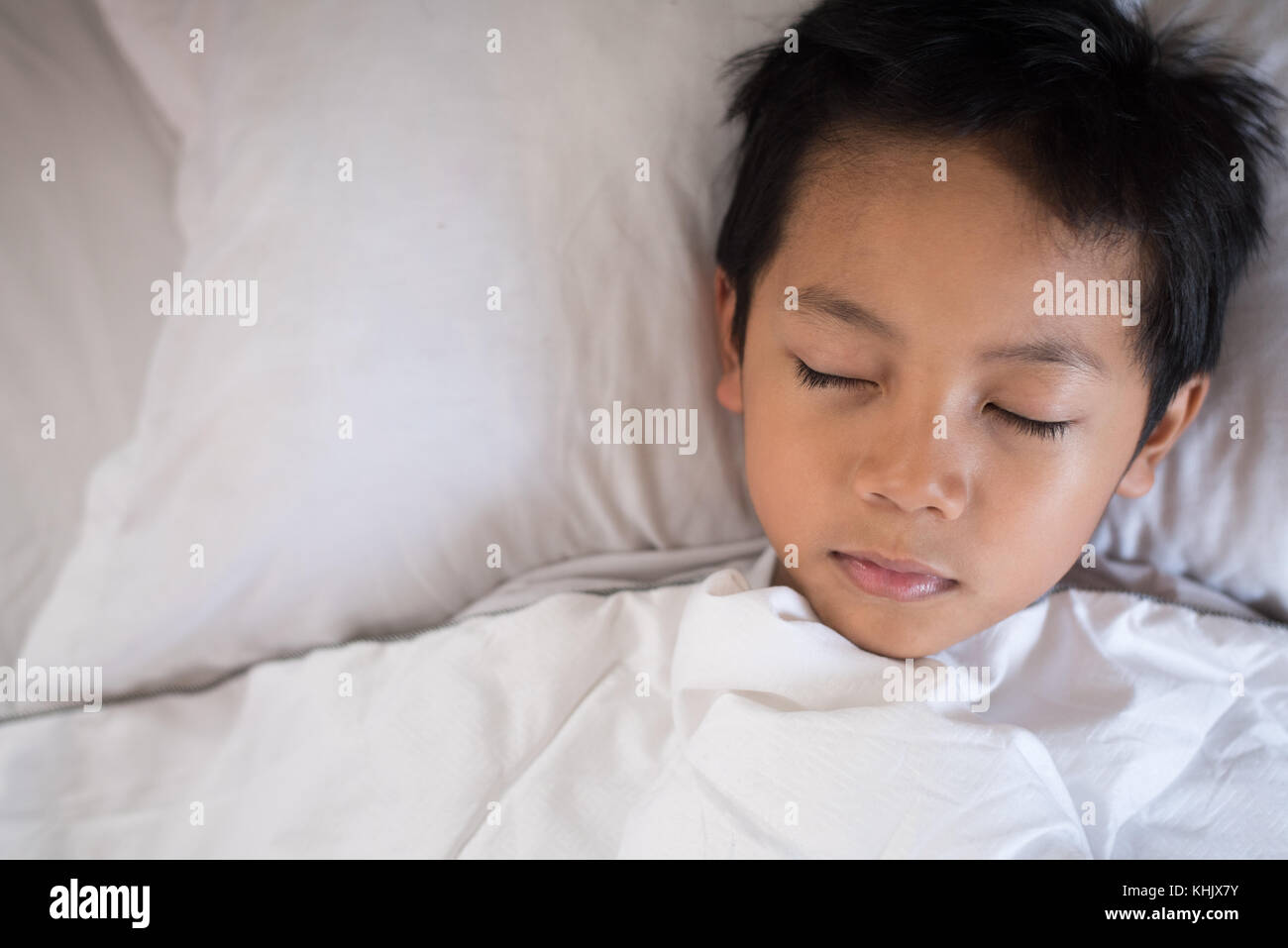 boy sleeping on bed with white sheet and pillow.asian kid fall asleep