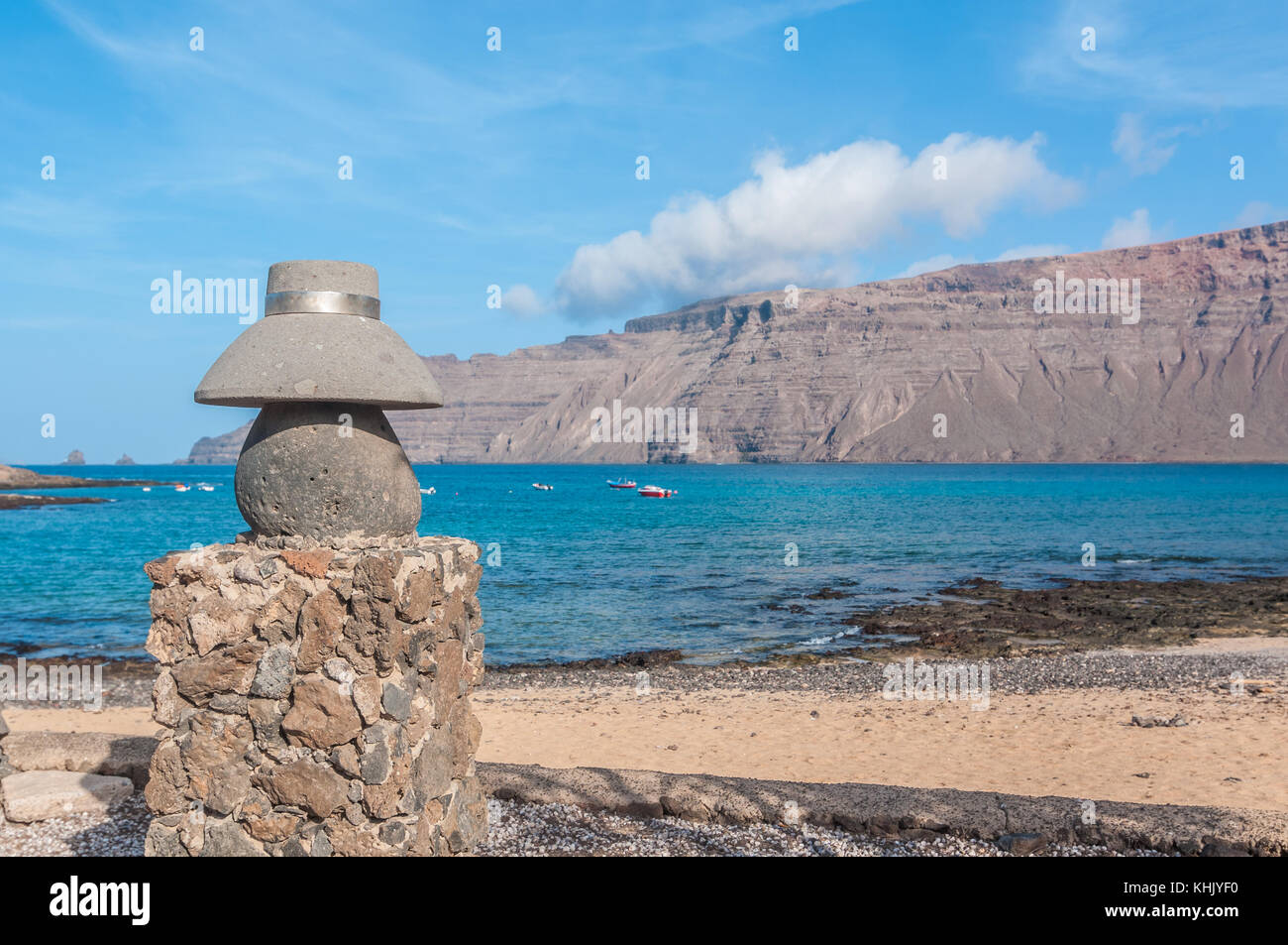 view of a typical street with a stone statue of a typical hat in the foreground and the beach in the background, La Graciosa, Canary Islands, Spain Stock Photo